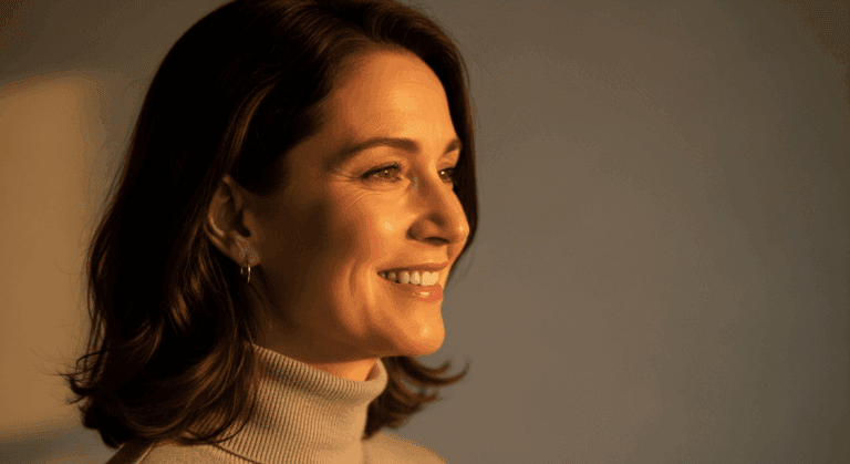 A smiling woman with shoulder-length dark hair wearing a turtleneck sweater, shown in a profile view.